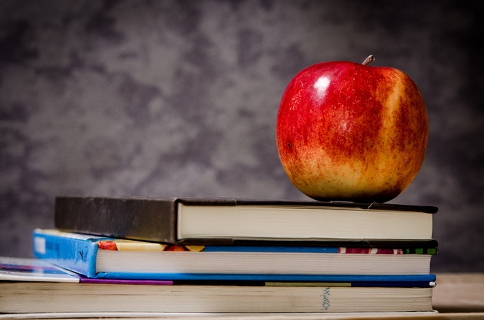 still life photo of a red apple places on top of books